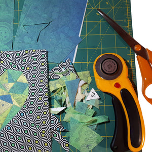 View of FPP heart work in process with rotary cutter, scissors and fabric scraps in greens and blues, by just.a.tad accessories, sold by Gems from Paradise.